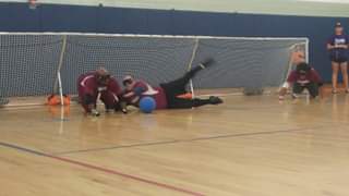 Three blindfolded people, on the ground playing goalball, trying to get the ball