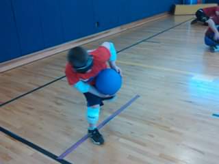 Blindfolded child playing goalball, about to throw the ball